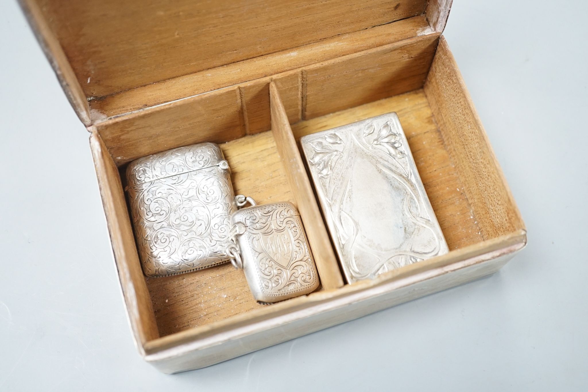 A silver mounted cigarette box, two silver vestas and a silver matchbox sleeve.